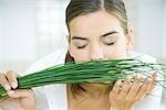 Young woman smelling a bunch of chives, eyes closed, head and shoulders