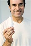 Man holding energy efficient light bulb, smiling at camera