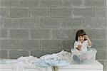 Little boy sitting in plastic storage container, laundry strewn beside him, pretending to drive