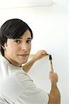 Man nailing thin piece of wood to wall, looking back over shoulder at camera