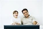 Father and son watching TV together, boy holding remote