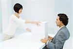 Professional woman and businessman exchanging tall stack of paper across desk