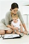 Professional woman sitting on the ground with toddler and agenda, dialing cell phone