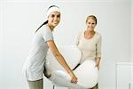 Mother and daughter carrying chair covered in bubble wrap, smiling at camera