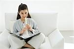 Girl sitting cross-legged on armchair, playing recorder