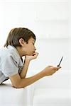 Boy looking at cell phone, hand under chin, side view