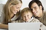 Family gathered around laptop computer, father and son smiling at camera