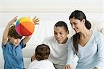 Family gathered around toddler girl, smiling, boy throwing ball in the air