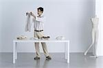 Man standing beside table, holding up sweater