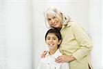 Grandmother standing behind grandson, both smiling at camera, portrait