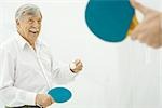 Senior man playing table tennis, hand holding paddle in foreground