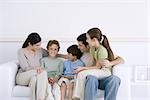 Family with three children sitting together on sofa, one boy smiling at camera