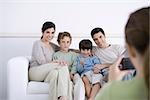 Family sitting on sofa, posing for photo being taken by daughter