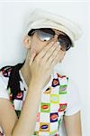 Teen girl wearing cap and sunglasses, covering mouth, portrait