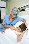Boy lying in hospital bed, sleeping, doctor holding stethoscope to boy's chest