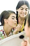 Young female friends looking at mirror, putting on make-up