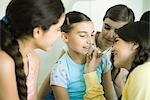 Young female friends putting make-up on younger girl