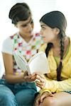 Young female friends reading book together, looking at each other