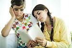 Young female friends reading book together