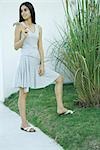 Woman standing by ornamental plant, looking over shoulder, full length portrait