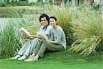 Couple assis sur l'herbe avec des livres, souriant à la caméra
