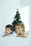 Knaben und Mutter auf dem Sofa, Weihnachtsbaum im Hintergrund, lächelnd in die Kamera, Stirnrunzeln junge Frau