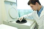 Young male researcher using centrifuge in laboratory, partial view