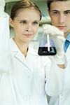 Young male and female scientists, woman holding up dropper and flask