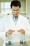 Researcher wearing protective goggles picking up Petri dish