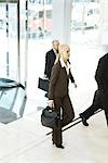Young businesswoman entering lobby, carrying briefcase, man in background
