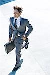 Young businessman running outdoors, carrying briefcase, smiling