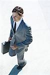 Young businessman walking outdoors, carrying briefcase, high angle view