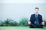 Businessman sitting on ground outdoors, meditating, eyes closed