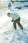 Young man bending over in snow, dodging snowball, full length