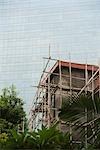 Bamboo scaffolding around building, glass facade of skyscraper in background