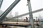 Cyclists and pedestrians on footbridge, cityscape in background