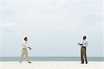 Two businessman walking toward each other on the beach, both smiling