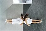 Two teenage girls sitting back to back on black and white divided floor, viewed from directly above