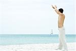 Homme debout sur la plage avec les bras levés, regardant la vue, vue latérale