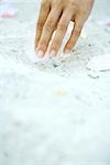 Hand picking up flower petal on sand, surface level view