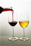 Two wine glasses, red wine being poured into one, white wine in the other