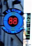 Le Club Multimedia neon sign with "Hotel" sign in background, blurred