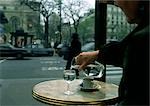 Person sitting at table on cafe terrace, pouring water from carafe