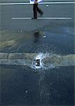 Pool of water on street and person walking, low section