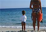 Mother and son standing on beach, looking at sea, rear view