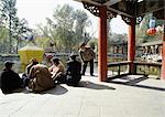 China, Xinjiang Province, Urumqi, group of men sitting on pagoda floor, park in background