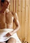 Bare-chested man sitting in sauna with eyes closed, blurred