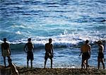 Silhouettes of people standing on beach at edge of sea, waves in background