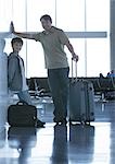 Father and son standing with suitcases in airport