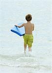 Boy running in surf at beach with body board